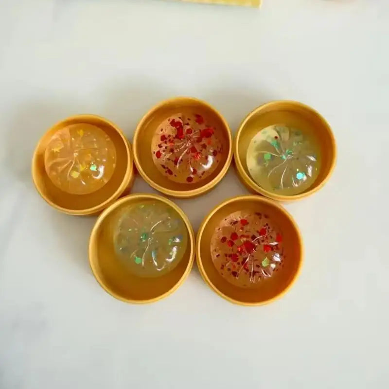Five mini soup dumpling squishies in their steamer cases, showing the different glitter colours.