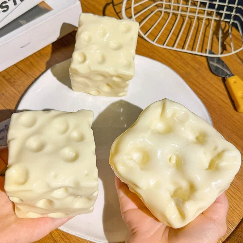Two pale cream cheese cube squishies with holes pressed into each face, resting on a plate.